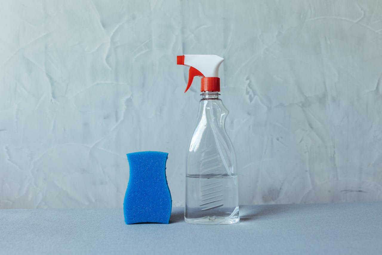 A spray bottle and blue sponge on a textured grey surface. Perfect for cleaning themes.