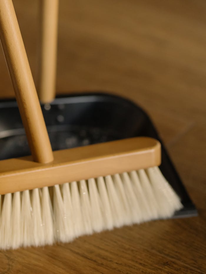 Detailed image of a broom and dustpan used for cleaning wooden floors at home.