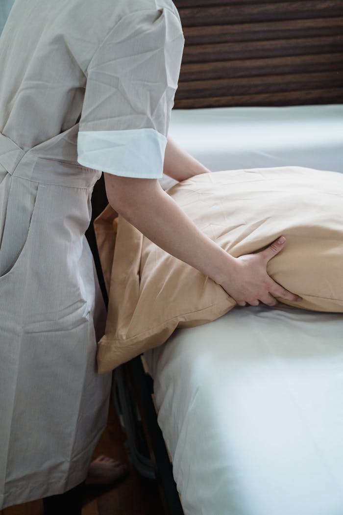 Hotel staff adjusting a pillow on a bed, ensuring guest comfort in a cozy room.